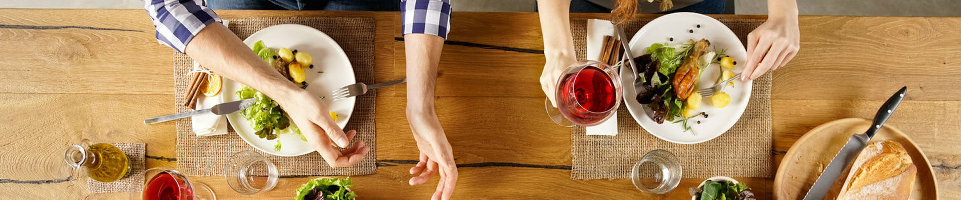 Photo of a dining table with 2 set of hands one holding a glass of red wine